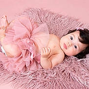 Lara is registered to the contest to win money with this photo: baby, infant, tutu, pink, fluffy_rug, hair_clip, cute, lying_down, soft_texture, pastel, child, portrait, adorable, skin, bare_chest, small_feet, curly_hair, studio_photo, indoor, young_child