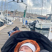 Liam a rejoint le concours — aidez-le/la à gagner de superbes lots ! baby, sleeping, stroller, pacifier, hat, jacket, marina, dock, boats, water, sky, cloudy, rope, wooden_pier, outdoor, calm, infant, transport, harbor, relaxation