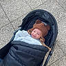 baby, stroller, hat, smile, child, outdoor, blanket, cozy, clothing, footwear, pavement, person, infant, cute, warm, headwear, happy, baby_carriage, portrait, baby_boy