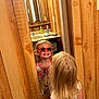 bathroom, blonde_hair, child, funny_glasses, happy, indoor, long_hair, mirror, person, playful, red_glasses, reflection, reflection_glasses, sink, smiling, soap_dispenser, standing, star_shaped_glasses, white_shirt, wood_paneling