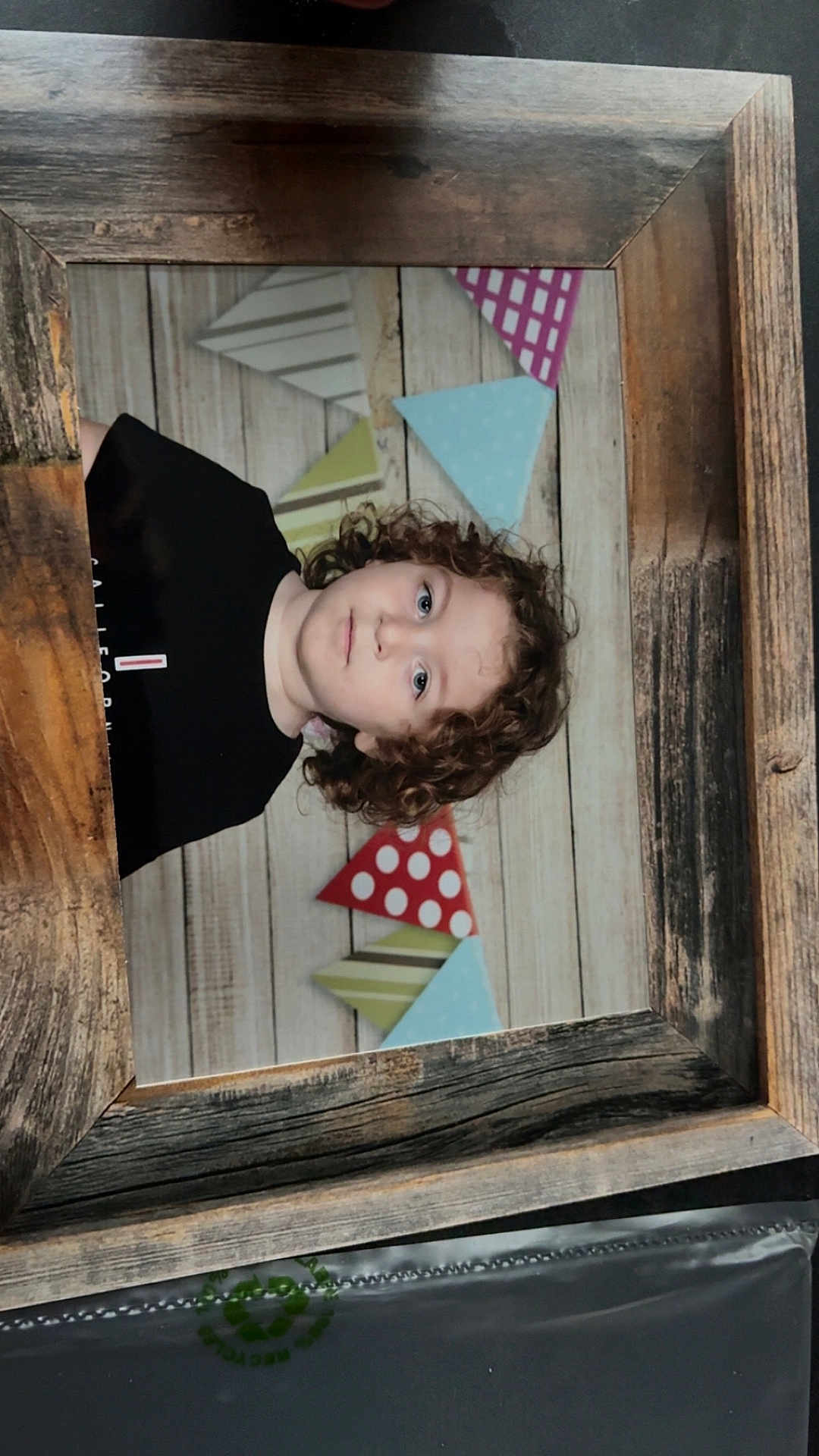 Lorenzo participe au concours pour gagner de l'argent avec cette photo : child, kid, portrait, curly_hair, wooden_frame, bunting, party_decor, background, photograph, face, eyes, neutral_expression, black_shirt, indoor, studio_style, headshot, framed_photo, wood_texture, polka_dot_pattern, cute
