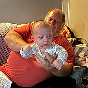 Kayce joined the competition — help win amazing prizes! baby, man, indoor, couch, blanket, clothing, person, holding, facial_expression, home, seated, smiling, pajamas, adult, child, relaxation, family, furniture, beard, casual