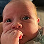 baby, close_up, hand, face, eyes, infant, skin, curious, indoors, warm_light, clothing, sleeve, newborn, portrait, cute, young_child, expression, fist, soft_focus, cozy