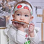 toddler, child, cookie, headband, holiday, christmas, gift, gift_box, white_clothing, indoor, face, hands, cute, festive, decoration, blurred_background, person, young_child, eating, holiday_season