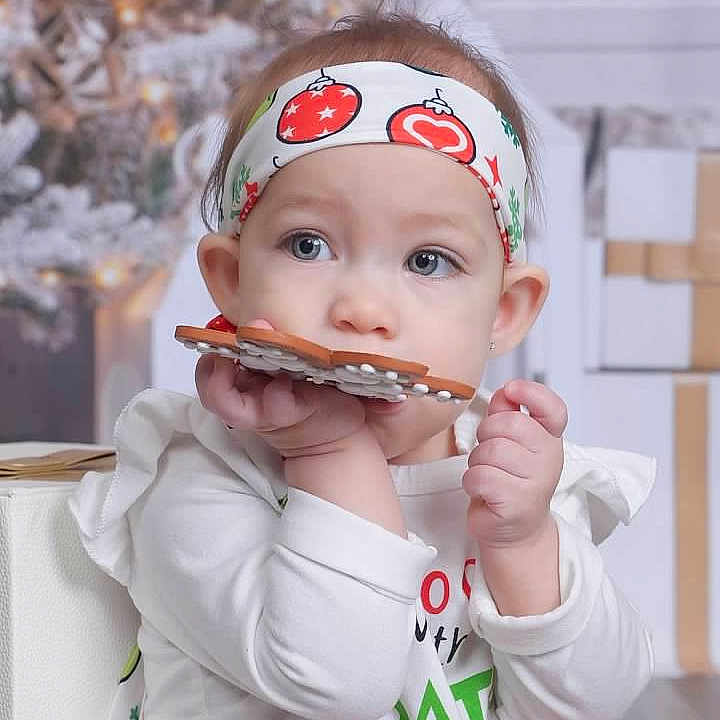 Zelda is registered to the contest to win money with this photo: blurred_background, child, christmas, cookie, cute, decoration, eating, face, festive, gift, gift_box, hands, headband, holiday, holiday_season, indoor, person, toddler, white_clothing, young_child