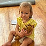 toddler, child, yellow_dress, teddy_bear, wooden_floor, sitting, indoor, cute, smiling, toy, barefoot, person, young_child, flooring, home, playtime, small_child, candid, happy, casual