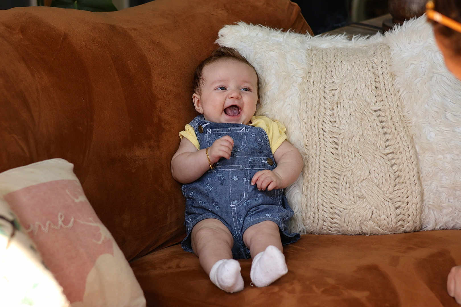 Rhaelynn is registered to the contest to win money with this photo: baby, infant, smiling, denim_overalls, yellow_shirt, white_socks, couch, brown_couch, pillow, knitted_pillow, fluffy_pillow, happy, indoor, person, child, seated, cute, home, cozy, portrait