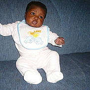 Aïsha participe au concours pour gagner de l'argent avec cette photo : baby, infant, bib, white_clothing, dolphin_design, couch, blue_background, sitting, arms_outstretched, cute, child, indoor, portrait, expression, face, person, young, comfortable, soft_fabric, home