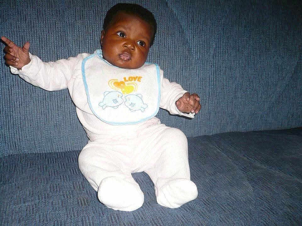 Aïsha participe au concours pour gagner de l'argent avec cette photo : baby, infant, bib, white_clothing, dolphin_design, couch, blue_background, sitting, arms_outstretched, cute, child, indoor, portrait, expression, face, person, young, comfortable, soft_fabric, home