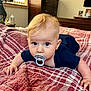 Justin is registered to the contest to win money with this photo: baby, pacifier, blanket, bed, indoor, child, portrait, face, blue_eyes, blond_hair, infant, cute, toddler, clothing, hand, furniture, room, window, curiosity, soft_light