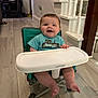 baby, child, high_chair, smiling, blue_shirt, indoor, wooden_floor, staircase, home, person, face, tray, foot, hand, furniture, happy, flooring, infant, sitting, casual