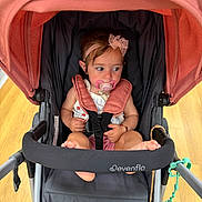 Araceli joined the competition — help win amazing prizes! baby, black, bow, child, curious, cute, evenflo, fabric, foot, hand, headband, indoor, infant, pacifier, person, pink, seat_belt, sitting, stroller, wooden_floor