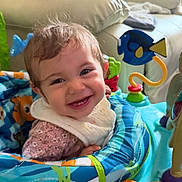 Araceli joined the competition — help win amazing prizes! activity_center, baby, bib, child, clothing, colorful, couch, cute, face, fish_toy, furniture, happy, indoor, infant, joyful, living_room, person, playful, smile, toy