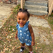 Reign is registered to the contest to win money with this photo: toddler, child, outdoor, grass, leaves, steps, porch, brick_wall, concrete, romper, polka_dot, smiling, hair_buns, sneakers, white_socks, happy, person, young_child, casual_clothing, daylight