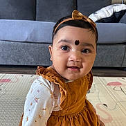 Manasvi is registered to the contest to win money with this photo: baby, bow, child, clothing, couch, cute, dress, face, floor, girl, happy, headband, home, indoors, long_sleeve, mat, pattern, portrait, sitting, smile