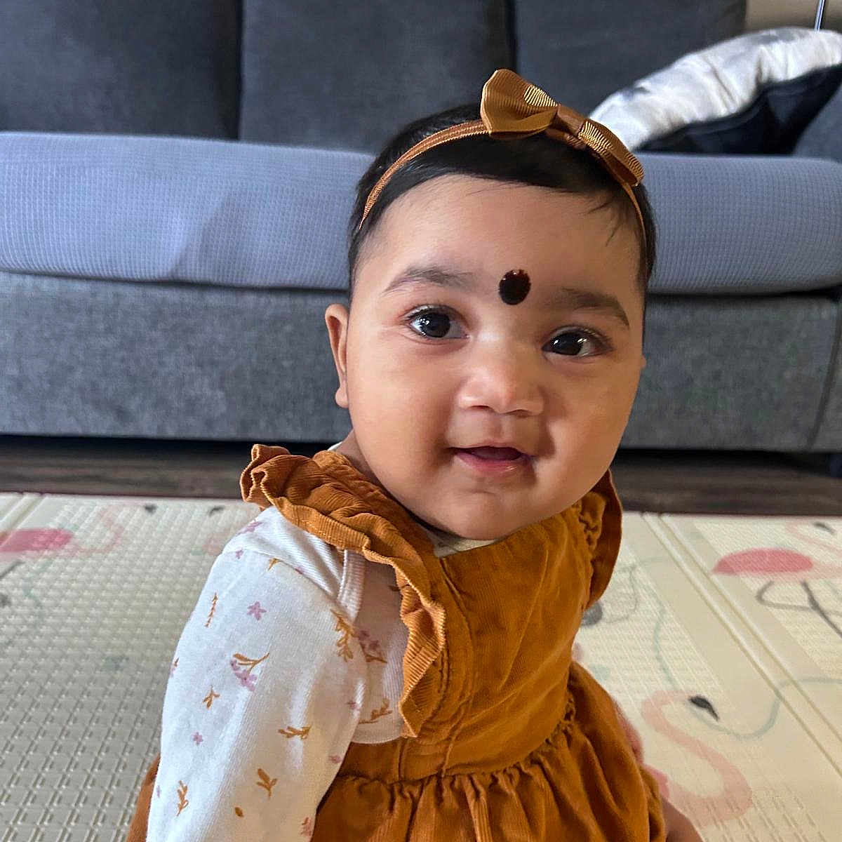 Manasvi is registered to the contest to win money with this photo: baby, bow, child, clothing, couch, cute, dress, face, floor, girl, happy, headband, home, indoors, long_sleeve, mat, pattern, portrait, sitting, smile