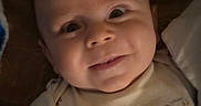 Mason is registered to the contest to win money with this photo: baby, infant, child, smiling, portrait, closeup, face, eyes, bed, bedding, pillow, onesie, clothing, indoor, cozy, lying_down, happy, cute, photograph, home