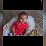 Amanuel is registered to the contest to win money with this photo: baby, smiling, red_shirt, basket, fluffy, wooden_floor, child, cute, happy, indoors, portrait, seated, infant, cozy, young_child, skin, hair, person, casual_clothing, comfortable