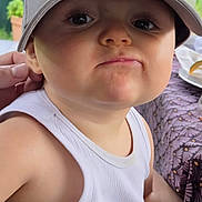 Antoine participe au concours pour gagner de l'argent avec cette photo : toddler, child, face, cap, white_tank_top, pout, expression, hand, table, tablecloth, food, plate, background, outdoor, person, clothing, skin, headwear, sitting, closeup