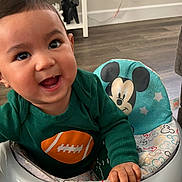 Anthony is registered to the contest to win money with this photo: baby, child, smiling, walker, toy, mickey_mouse, green_clothing, indoor, floor, happy, face, hand, furniture, living_room, playtime, cute, young_child, person, seat, colorful