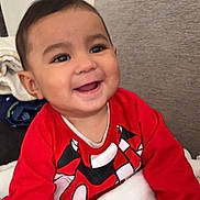 Anthony is registered to the contest to win money with this photo: baby, child, smiling, red_shirt, blanket, cartoon, indoor, couch, happy, face, person, toddler, clothing, infant, cute, young_child, home, portrait, sitting, cozy