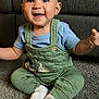 Anthony is registered to the contest to win money with this photo: baby, blue_shirt, carpet, child, cute, eyes, face, feet, furniture, green_clothing, hands, happy, indoor, mickey_mouse, overalls, person, sitting, smiling, sock, young_child