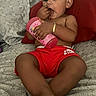 toddler, child, red_shorts, bottle, bed, pillow, indoor, relaxed, skin, foot, hand, face, person, casual, young_child, sitting, comfort, home, cute, young