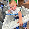 baby, child, shopping_cart, indoor, clothing, jeans, shirt, hand, face, blue_eyes, floor, store, retail, curious, rosy_cheeks, expression, person, footwear, shopping, seat_cover