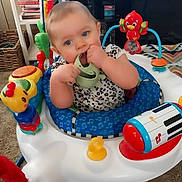 Freya is registered to the contest to win money with this photo: activity_center, baby, blue_eyes, bookshelf, carpet, child, colorful, face, indoor, infant, living_room, octopus_toy, piano_toy, play_mat, portrait, sitting, smiling, teething_toy, television, toy