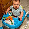 baby, baby_gear, blue_clothing, blue_walker, child, face, family, indoor, infant, kitchen, photography, plaything, portrait, seated, serious_expression, short_hair, tile_floor, toy, walker, wooden_cabinet