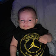 ézio participe au concours pour gagner de l'argent avec cette photo : baby, black, blur, child, clothing, cute, face, hand, head, indoor, infant, logo, lying_down, person, pillow, portrait, soft_lighting, tshirt, yellow, young