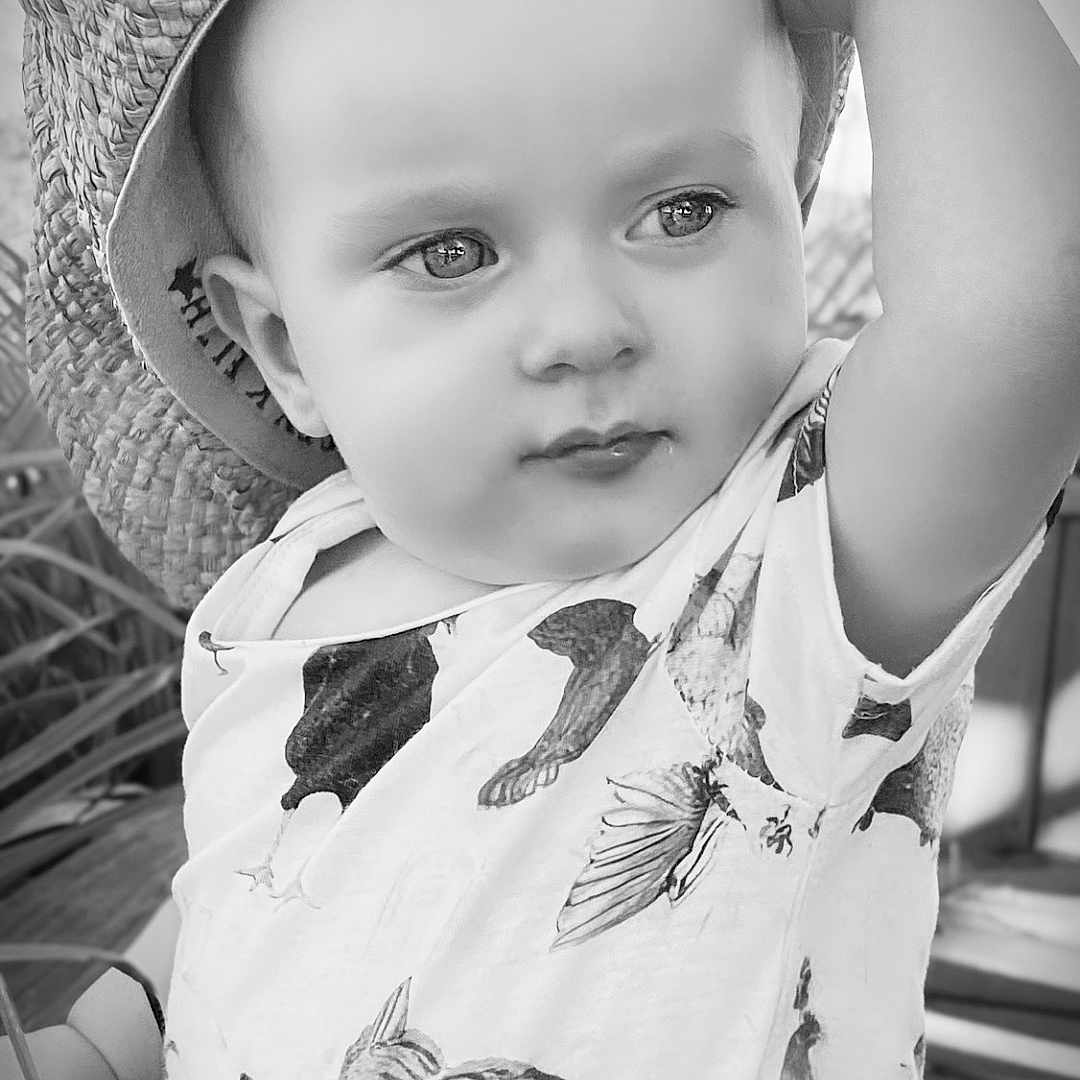 Jerry Westyn is registered to the contest to win money with this photo: baby, child, portrait, black_and_white, sunhat, hat, smiling, face, eyes, sitting, outdoor, garden, patio, clothing, patterned_outfit, birds, chickens, fashion, close_up, happy