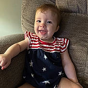 Isabelle is registered to the contest to win money with this photo: baby, infant, child, smiling, happy, sitting, armchair, clothing, stars, stripes, red, white, blue, face, tongue, cute, indoors, furniture, portrait, person
