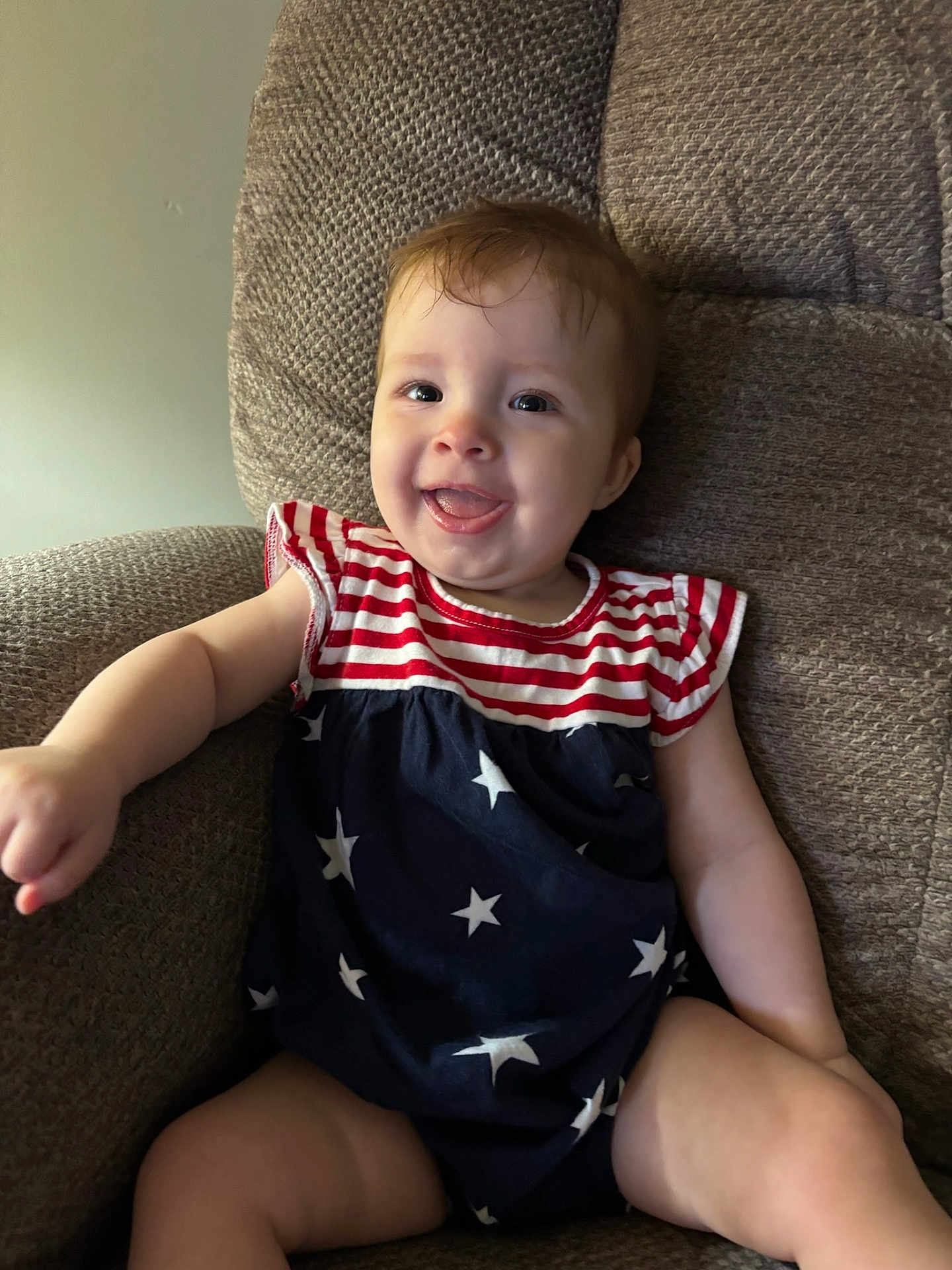 Isabelle is registered to the contest to win money with this photo: baby, infant, child, smiling, happy, sitting, armchair, clothing, stars, stripes, red, white, blue, face, tongue, cute, indoors, furniture, portrait, person