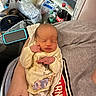 baby, bag, blanket, bottle, child, clothing, coca_cola, face, hands, home, indoor, infant, lap, newborn, onesie, photograph, portrait, relaxed, sitting, sleeping