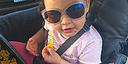 Melinda is registered to the contest to win money with this photo: baby, car, casual, child, chips, daylight, face, food, hand, outdoor, parking_lot, person, pink_clothing, seat, seatbelt, smile, snack, stroller, sunglasses, toddler