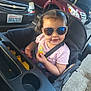 Melinda is registered to the contest to win money with this photo: baby, black_stroller, car, casual, child, chips, concrete, cute, messy_face, outdoor, parking_lot, pink_shirt, seatbelt, smiling, snack, stroller, sunglasses, sunshine, toddler, vehicle