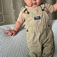 Samuel joined the competition — help win amazing prizes! baby, child, overalls, beige, couch, curtains, string_lights, brown_shoes, standing, indoors, portrait, cute, face, hand, footwear, fabric, texture, lighting, clothing, expression