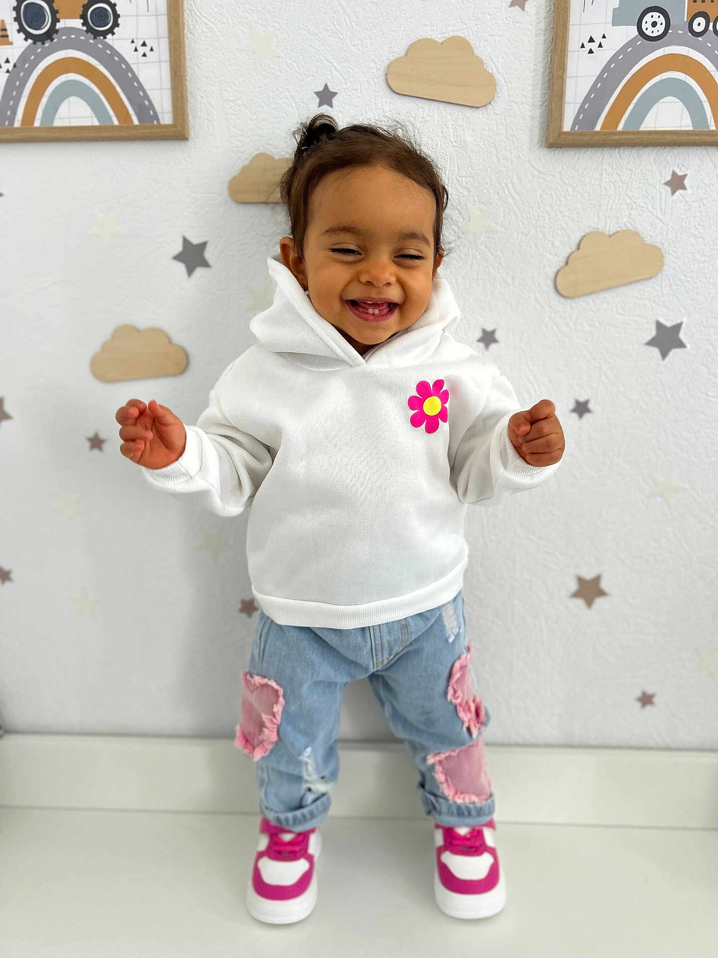 Naïla a rejoint le concours — aidez-le/la à gagner de superbes lots ! toddler, child, smiling, white_hoodie, pink_flower, jeans, pink_patches, sneakers, pink_and_white, standing, wooden_clouds, star_stickers, wall_art, rainbow, indoor, happy, cute, person, portrait, fashion