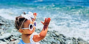 Naïla participe au concours pour gagner de l'argent avec cette photo : toddler, child, beach, rocks, ocean, waves, sunlight, sunglasses, white_top, checkered_shorts, headband, bow, summer, playful, outdoor, water, sky, vacation, cute, sunny