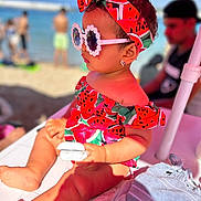 Naïla participe au concours pour gagner de l'argent avec cette photo : toddler, child, beach, sunglasses, headband, watermelon_pattern, summer, sunny, outdoor, fashion, person, earrings, skin, hand, foot, seat, accessory, vacation, relaxation, colorful