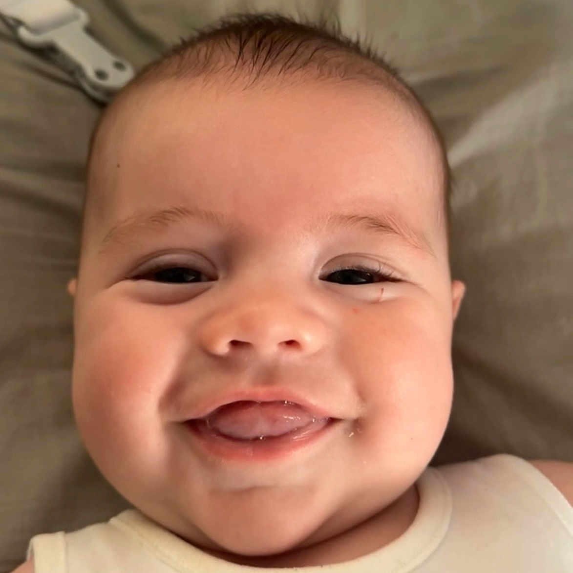 Luca Allan Hendrix is registered to the contest to win money with this photo: baby, child, chubby_cheeks, close_up, cute, expression, eyes, face, happy, head, indoor, infant, lying_down, mouth, person, skin, smiling, soft_background, tongue, white_clothing