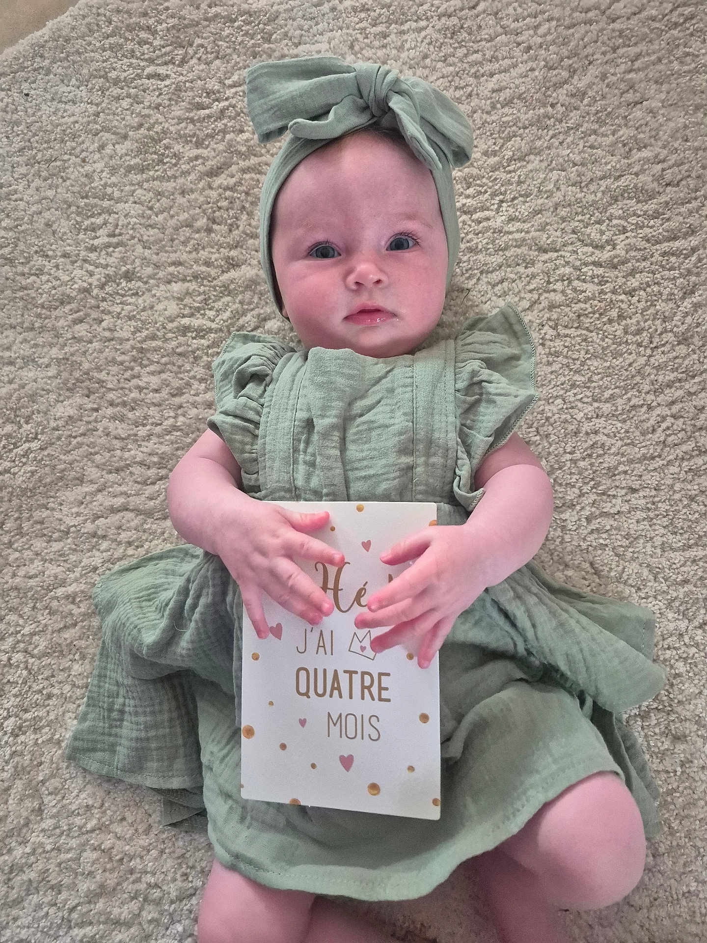 Lison participe au concours pour gagner de l'argent avec cette photo : baby, infant, milestone_card, green_dress, headband, carpet, lying_down, hands, cute, child, portrait, indoors, soft_texture, milestone, four_months, person, young_child, expression, skin, clothing