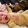 baby, bed, blanket, calico_cat, cat, close_up, cozy, cuddling, face, floral_pattern, hand, happy, infant, mouth_open, nursery, onesie, pet, pillow, smiling, yellow