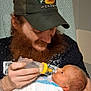 Larry joined the competition — help win amazing prizes! man, baby, feeding, bottle, beard, hat, tattoo, arm, newborn, hospital, blanket, chair, intimate, indoor, person, holding, caring, portrait, love, family