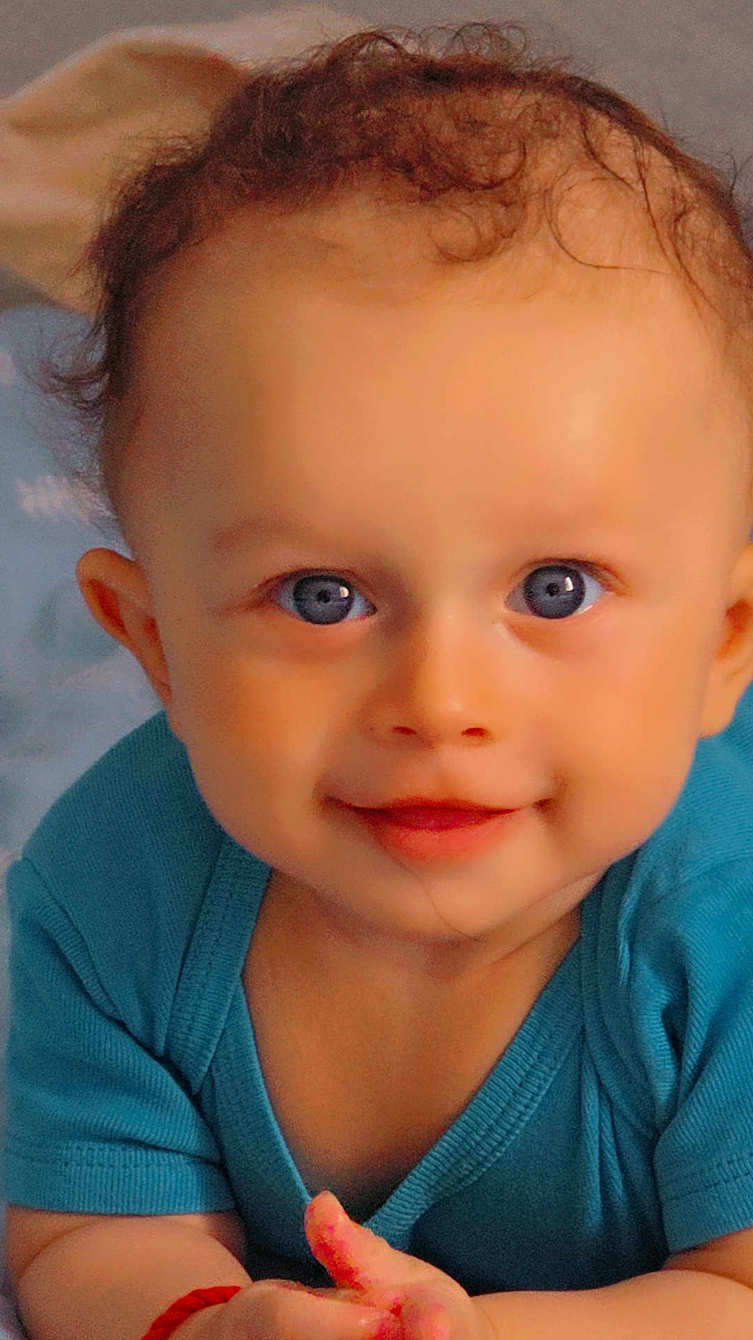 Leeroy participe au concours pour gagner de l'argent avec cette photo : baby, child, blue_eyes, curly_hair, smiling, portrait, close_up, infant, cute, happy, young_child, skin, face, clothing, sitting, expression, blue_shirt, hands, looking_at_camera, indoors