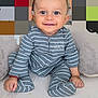 baby, smiling, child, onesie, striped_clothing, blue_eyes, sitting, plush_cushion, indoor, happy, cute, portrait, infant, soft_fabric, hands, feet, cozy, face, person, young_child