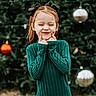 child, girl, smile, green_sweater, hair_bows, cheeks, portrait, outdoor, holiday_decorations, blurred_background, playful, young, happy, cute, festive, fun, person, long_hair, expression, casual_clothing