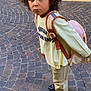 Ismail a rejoint le concours — aidez-le/la à gagner de superbes lots ! child, curly_hair, backpack, pavement, cobblestone, shirt, pants, sneakers, outdoor, expression, side_view, young, urban, standing, casual_clothing, person, looking_up, building, door, yellow_chair