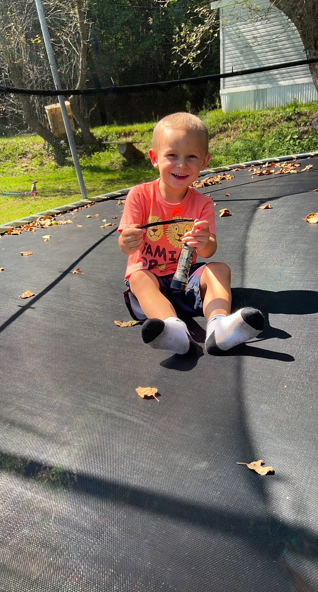 Braxton is registered to the contest to win money with this photo: asphalt, child, city, fun, grass, joy, leisure, person, plant, play, recreation, road_surface, rope, shorts, sidewalk, sitting, smile, sneakers, t_shirt, toddler